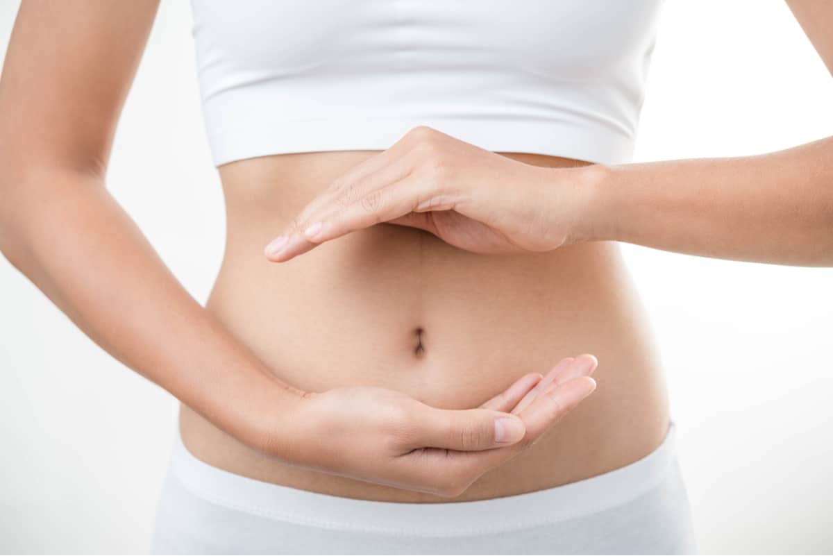 Woman in white with hands around her stomach indicating digestion