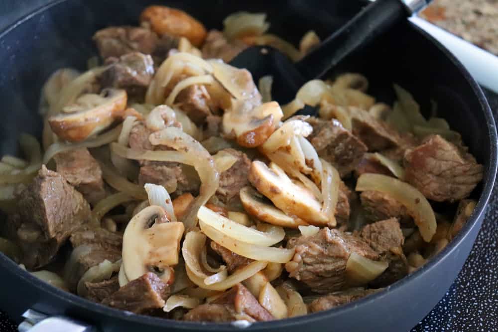 Adding beef and onions to mushrooms