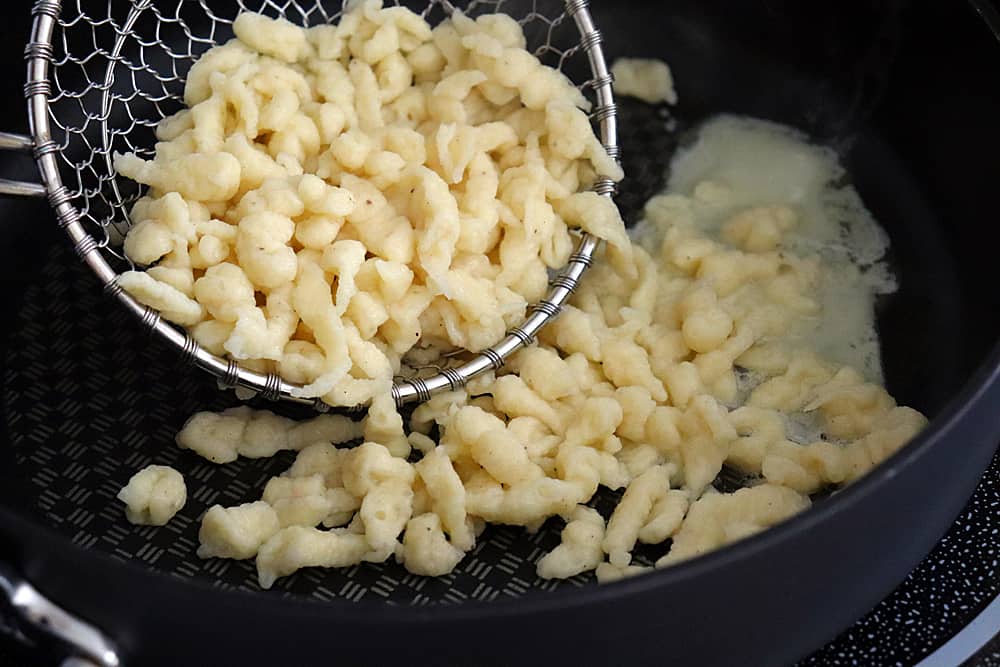 Adding boiled spaetzle to the pan with butter