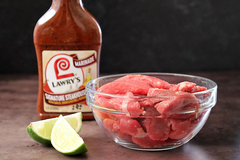 Steak cut into strips with a bottle of Lawry's marinade